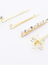 Set de cuatro hebillas para el pelo doradas con diferentes diseños: una con strass, una con perlas y una con forma de flor.
