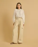 Pantalón acampanado color beige con pinzas, bolsillos italianos y bolsillos de parche con solapas en los laterales. Cierre con botones y cintura con trabillas.