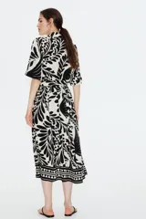 Vestido midi camisero con estampado floral en blanco y negro, cuello camisero, botonadura frontal y mangas cortas. Incluye cinturón extraíble para atar.