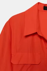 Vestido midi camisero color ladrillo, confeccionado en popelina de algodón. Presenta cuello solapa, manga corta con puños abotonados, bolsillos laterales ocultos y bolsillos de parche con solapa en el pecho. Incluye cinturón lazada en el mismo tejido y cierre frontal con botones ocultos.