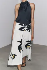 Falda midi de tiro alto confeccionada en hilatura de algodón color blanco con estampado floral en negro y amarillo. Tiene cierre con cremallera oculta en la costura y detalle de botones en la cintura.