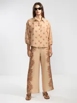Pantalón palazzo color beige con estampado de girasoles marrones en el ruedo.