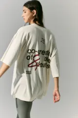 Remerón de jersey de algodón color crudo, de manga corta, con estampa en serigrafía en frente y espalda con la frase "co-creator of love & dreams" y un arco y flecha.