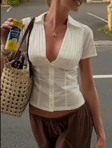 Camisa blanca entallada con cuello clásico, mangas cortas y cierre frontal con botones.