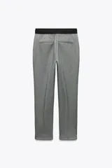 Pantalón gris de vestir, de corte tobillero, con tiro medio, cintura elástica en la parte trasera, bolsillos delanteros y falsos bolsillos traseros.