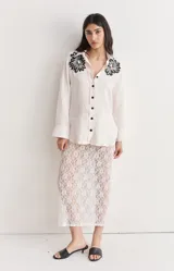 Camisa de lino color blanco con bordado de flores negras en los hombros y abertura en los laterales.