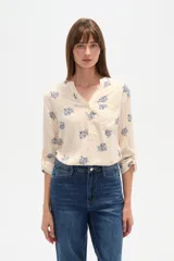 Blusa de manga tres cuartos color crema con estampado floral en azul. Presenta cuello mao con abertura en V y un bolsillo de parche en el pecho.