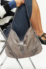 Cartera tipo hobo de cuero vegano, con hebillas decorativas y diseño estilizado.