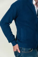 Cárdigan azul de punto con cuello alto, cierre frontal con cremallera y bolsillos laterales.