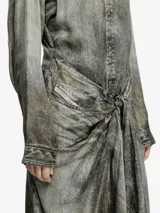 Vestido largo tipo camisa, color gris oscuro con efecto desgastado/decolorado, manga larga y cuello camisero. La prenda se anuda a la altura de la cintura, creando un efecto drapeado asimétrico en la falda.