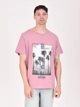 Remera de algodón color rosa con estampado de palmeras y texto en el frente.