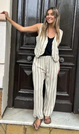 Conjunto de lino color crema con rayas verticales negras, compuesto por un chaleco con botones y un pantalón de corte recto con cintura elastizada y cordón ajustable.