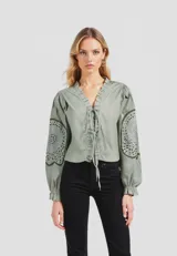 Blusa color verde agua con escote en V con volados y lazo ajustable. Presenta mangas largas abullonadas con apliques de encaje calado.