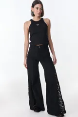 Pantalón de jean negro de pierna ancha con cortes en los laterales que van desde la pretina al bajo del pantalón. Por la mitad de la pierna presenta godets triangulares de encaje para darle mayor amplitud y detalles a la prenda.