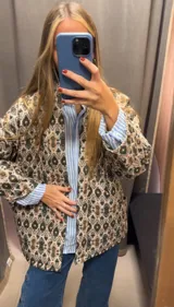 Chaqueta con estampado de arabescos en tonos marrones, beige y negro, con cuello mao, mangas largas y lazo para ajustar en la cintura.