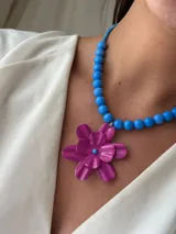 Collar corto de cuentas celestes con dije de flor fucsia.