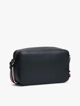 Cartera cruzada tipo cámara de poliuretano color azul marino, con cierre principal de cremallera y monograma TH metálico dorado al frente. La correa larga es ajustable y presenta la cinta distintiva de la marca en rojo, blanco y azul.