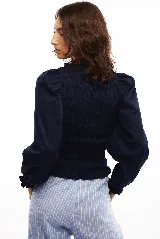 Blusa blanca de algodón con frunces tipo smock en el cuerpo, cuello redondo y mangas largas abullonadas con puños elásticos.