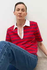 Remera de manga corta con cuello polo blanco y escote pronunciado en V. El cuerpo de la prenda es de color rojo con finas rayas horizontales en azul oscuro y azul claro.