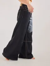 Pantalón ancho negro de algodón y lino con costuras en color mostaza, pinzas debajo de la rodilla y bordado de monograma en el bolsillo delantero.
