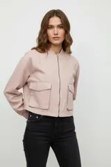 Campera corta color beige, estilo bomber, de manga larga y cierre frontal con cremallera. Tiene dos bolsillos con solapa en el pecho.