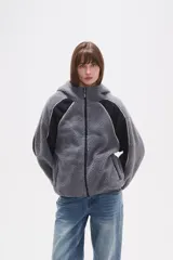 Campera de abrigo de tejido polar (tipo sherpa) color gris oscuro, con capucha y cierre frontal. Presenta paneles de color negro en los hombros y mangas, ribeteados con un vivo de color claro.