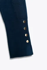 Jersey negro de punto liso con cuello alto, manga larga y detalle de botones dorados en los puños.