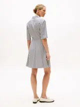 Vestido corto camisero a rayas verticales blancas y azules, con cuello clásico, mangas cortas y nudo en la cintura.