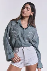 Camisa celeste con bordado de hojas blancas en el frente, de corte clásico y mangas largas.