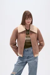 Campera negra de estilo aviador, confeccionada en material tipo gamuza o suede, con cuello y forro de corderito (shearling) negro. Presenta cierre frontal metálico y puños y ruedo con terminación de corderito.