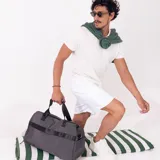 Bolso deportivo de mano color gris, con doble asa corta y correa larga regulable. Cuenta con bolsillos exteriores con cierre.