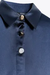 Camisa azul marino de satén con cuello solapa y manga larga. Cierre frontal con botones ocultos por solapa y botones dorados con relieve.