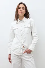 Camisa de jean color crudo, estilo western, con cuello y dos bolsillos frontales con tapa y botón. Presenta costuras contrastantes en tono rojizo.