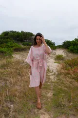 Túnica de corte holgado con estampado a cuadros en tonos rosa y crudo, con cuello redondo y mangas cortas amplias. Incluye cinturón de la misma tela para ajustar a la cintura.