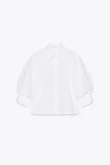 Camisa blanca de algodón con cuello solapa y mangas cortas abullonadas. Cierre frontal con botones.