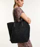 Bolso de playa negro tejido en paja de papel, con asas de hombro en cuero sintético y detalle de borla colgante.