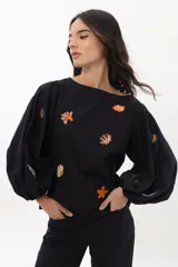 Blusa color arena de algodón con escote a la base y mangas abullonadas. Presenta bordados artesanales de motivos marinos en tonos naranja y azul.
