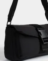 Bandolera negra de tela deportiva con correa regulable y desmontable, solapa con broche a presión y hebilla frontal con estampa.