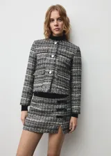 Chaqueta corta de tweed con cuello redondo, cierre frontal con botones metálicos y cuatro bolsillos de solapa.