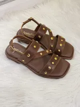 Sandalias bajas de cuero marrón con tiras cruzadas y apliques de tachas doradas.