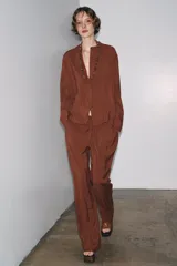 Camisa marrón de Zara Woman Collection confeccionada en hilatura con mezcla de lyocell. Tiene cuello redondo, manga larga acabada en puño, bajo asimétrico con aberturas laterales y cierre frontal con botones.
