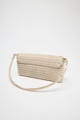 Bolso alargado color beige con diseño trenzado, asa bandolera y tirador con pulsera de mano. Incluye bolsillo interior y cierre mediante solapa y botón imantado.