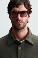 Sobrecamisa color beige de corte relaxed fit, confeccionada en tejido con elasticidad. Tiene cuello solapa, manga larga con puños abotonados, bolsillos de parche con solapa en el pecho y bolsillos de ojal en la cadera. El cierre es frontal con botones.