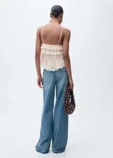 Pantalón de jean celeste de corte wide leg, tiro alto, con cinco bolsillos, cierre con cremallera y botón, trabillas y bajo deshilachado. Incluye un cinturón de cadena plateada con dije de flor.