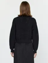 Conjunto de buzo y vestido negro marca Current Air. El vestido es de satén con escote en V y falda plisada. El buzo es de tejido calado, liviano y delicado.