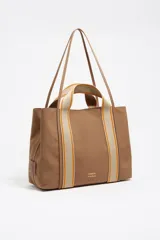 Bolso shopper grande de estructura blanda, color marrón, confeccionado en nylon con detalles de piel vacuna. Presenta doble asa de mano con cinta de tejido beige y naranja, y un logo metálico de Bimba y Lola en el frente.