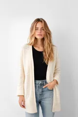 Saco de tejido de punto color natural o crema, de corte holgado y largo, con manga larga y bolsillos frontales. Presenta un tejido calado con patrones en forma de espiga o chevron.