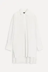 Camisa extra larga blanca de popelín de algodón, con cuello solapa, manga larga con puños, pinzas en la espalda, aberturas laterales y cierre frontal con botones.