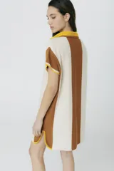Vestido corto tejido en jersey liviano de algodón y acrílico, con diseño tipo polo y fit holgado. Presenta rayas verticales en color marrón y crudo, bordado XL de un ají y terminaciones en color amarillo.