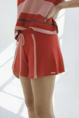Short tejido en jersey color crudo con cintura elastizada azul marino y cordón rojo. Presenta rayas verticales rojas y laterales en azul marino.